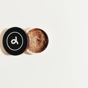 A minimalist photograph showcasing an open jar of coffee scrub on a clean white backdrop.