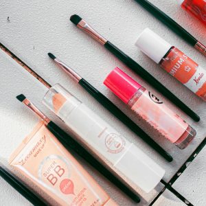 Flatlay image showcasing various makeup products and brushes arranged on a white surface, ideal for beauty themes.