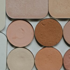 Flat lay of various makeup powders and eyeshadows, showcasing different warm nude shades.