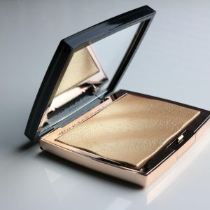 Golden makeup compact open on a glossy white surface, highlighting elegance.