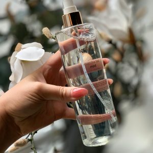 Detailed shot of a hand holding a cosmetic spray bottle surrounded by white flowers.